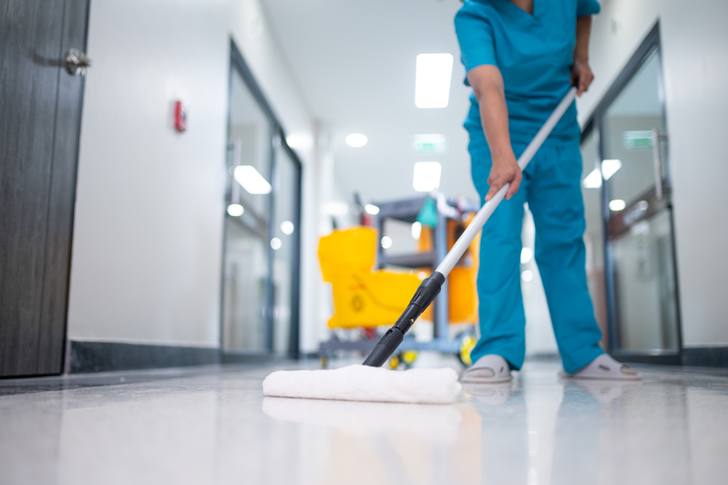 清潔人員正在對辦公室地板進行打蠟，地板左側已打蠟區域顯得光亮，右側未打蠟區域則較為暗沉，展現地板打蠟前後差異，凸顯地板打蠟費用價值。